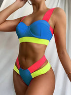 Modelo vestindo biquíni azul com rosa e verde neon, top estruturado e calcinha cavada com tiras duplas coloridas.