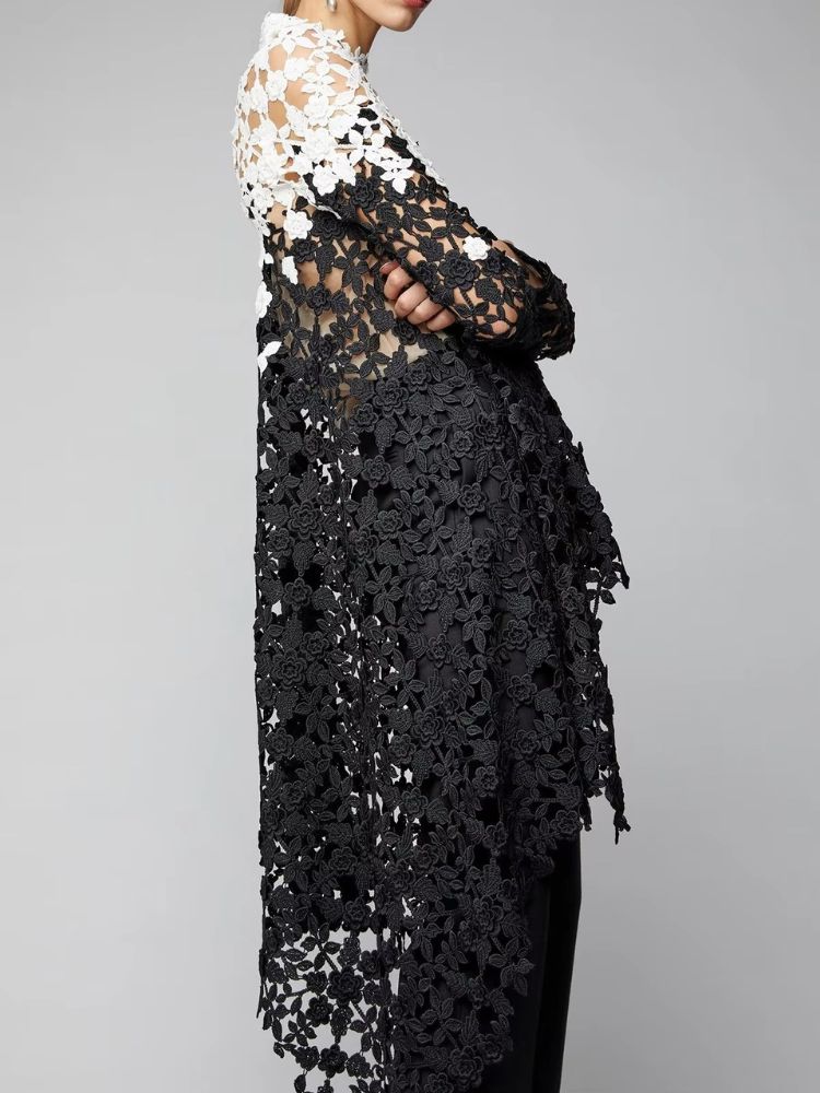 Blusa assimétrica feminina em renda vazada preta e branca vista de lado, mostrando detalhe floral tridimensional e transparência elegante.