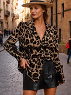 Mulher posando em rua de paralelepípedos usando blusa de estampa leopardo de mangas longas e shorts de couro preto, com chapéu claro.
