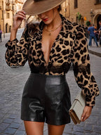 Mulher usando blusa de estampa leopardo com decote profundo e mangas longas bufantes, combinada com shorts de couro preto em rua urbana.