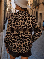 Vista traseira de mulher usando blusa de estampa leopardo com mangas longas e detalhe de transição de tons, em rua de paralelepípedos.