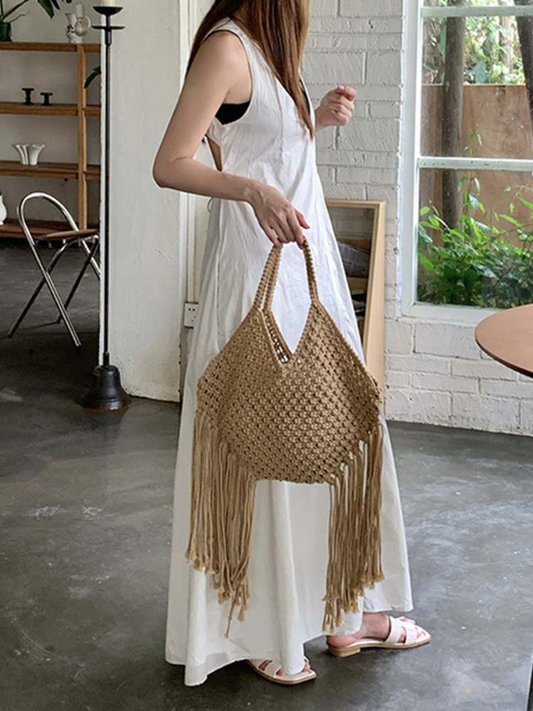 mulher segurando bolsa de macramê bege com franjas longas combinada com vestido branco

