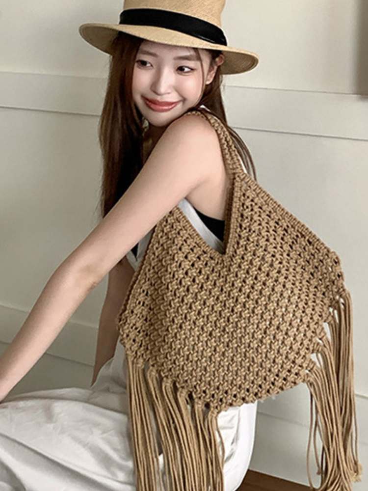 bolsa de macramê bege com franjas usada no ombro por modelo com chapéu de palha
