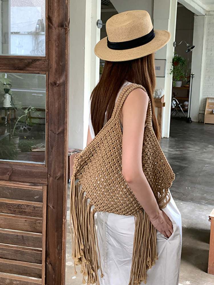 vista traseira de bolsa de macramê bege com franjas sendo usada com vestido longo branco
