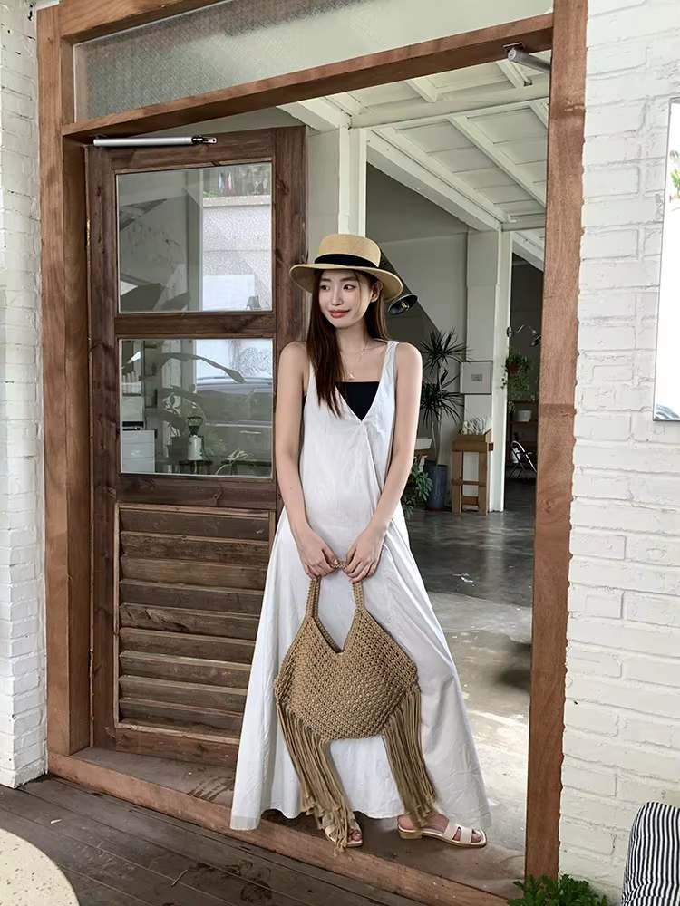 modelo com vestido branco segurando bolsa de macramê bege com franjas na porta de madeira
