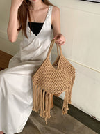 bolsa de macramê bege com franjas sendo segurada por modelo sentada
