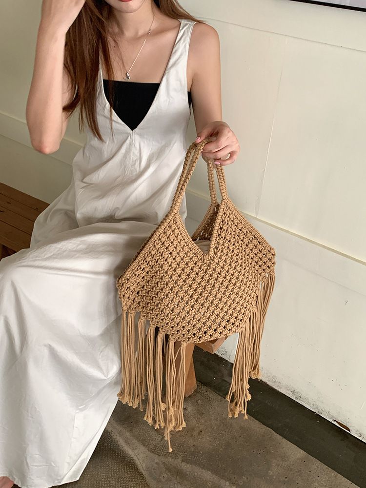 bolsa de macramê bege com franjas sendo segurada por modelo sentada
