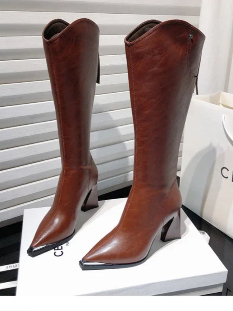 Par de botas femininas de cano alto em couro marrom com bico fino e salto bloco, expostas sobre uma caixa branca.