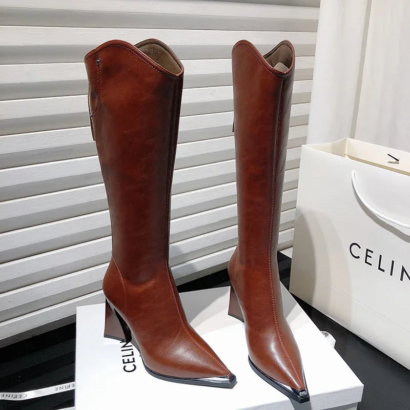Par de botas femininas marrons de cano alto sobre caixa, com acabamento em couro e bico fino metálico.