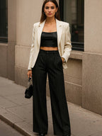 Look feminino com calça preta de risca de giz, blazer claro e top preto em ambiente urbano