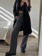 Calça feminina de alfaiataria larga cinza com risca de giz, modelo reto, fotografada em frente ao espelho com casaco preto
