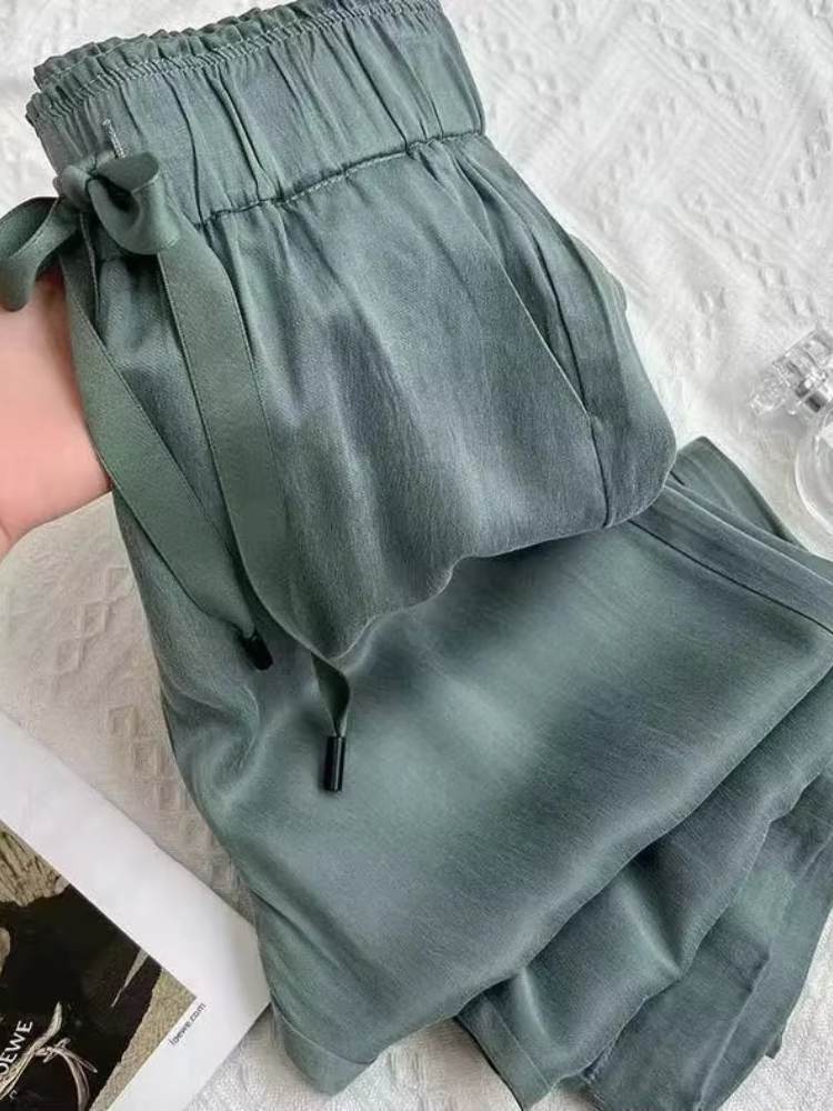 Calça feminina verde em tecido acetinado sendo segurada pela cintura, mostrando textura leve e brilhante.