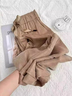 Calça feminina bege em tecido leve e acetinado, com cós elástico e laço, sendo segurada para mostrar o caimento fluido.