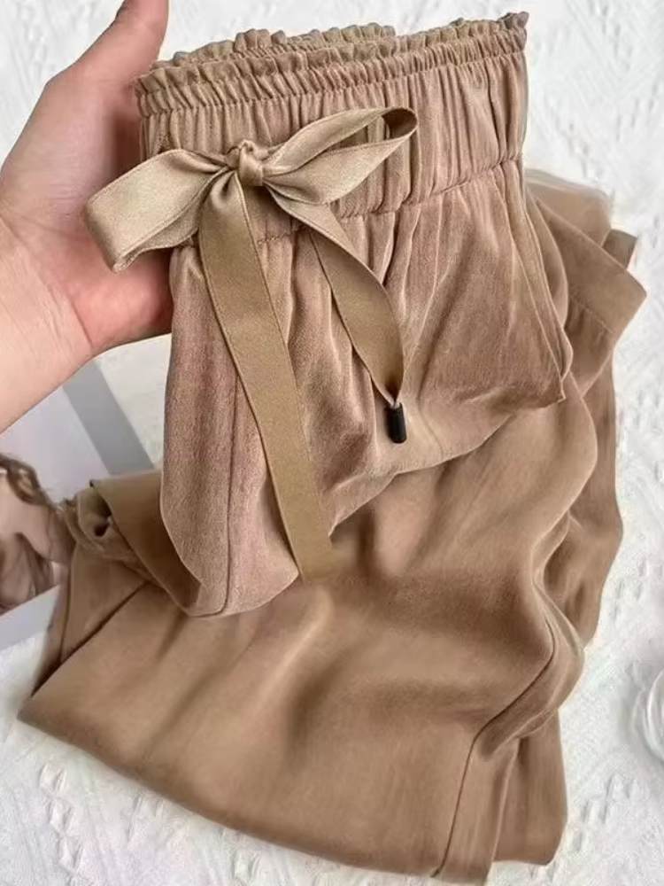 Detalhe da cintura da calça feminina bege em tecido acetinado, com elástico e laço firme frontal.