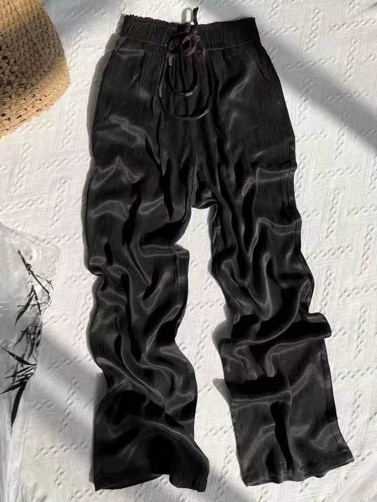 Calça feminina preta ampla esticada em superfície clara, evidenciando brilho e textura do tecido.