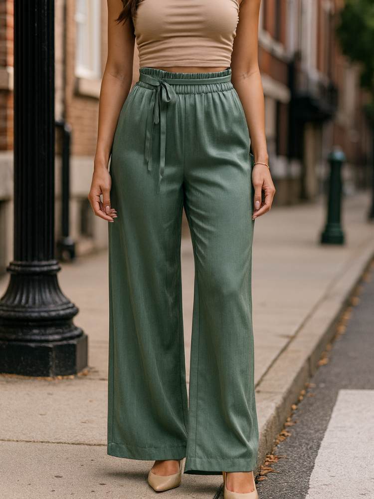 Modelo usando calça verde ampla de tecido acetinado, cintura alta com amarração frontal, em ambiente urbano.