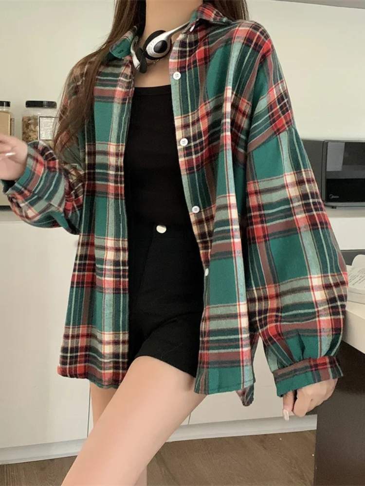 Camisa xadrez feminina em tons de verde, vermelho e creme, modelagem oversized, usada aberta sobre top preto e shorts preto, estilo casual moderno.