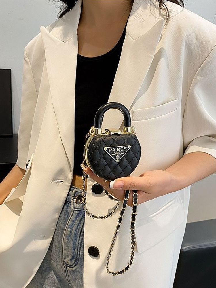 Mulher usando blazer claro segurando uma mini bolsa preta em formato de cadeado com detalhes dourados e corrente de ombro.