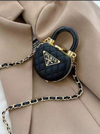 Mini bolsa preta acolchoada em formato de cadeado com corrente dourada sobre um blazer bege