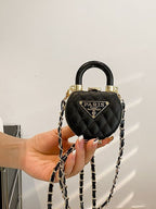 Mini bolsa preta acolchoada em formato de cadeado sendo segurada pela alça superior, exibindo corrente dourada