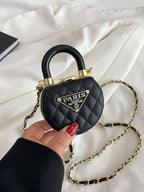 Mini bolsa preta acolchoada com detalhes dourados sendo segurada na mão sobre um tecido claro.