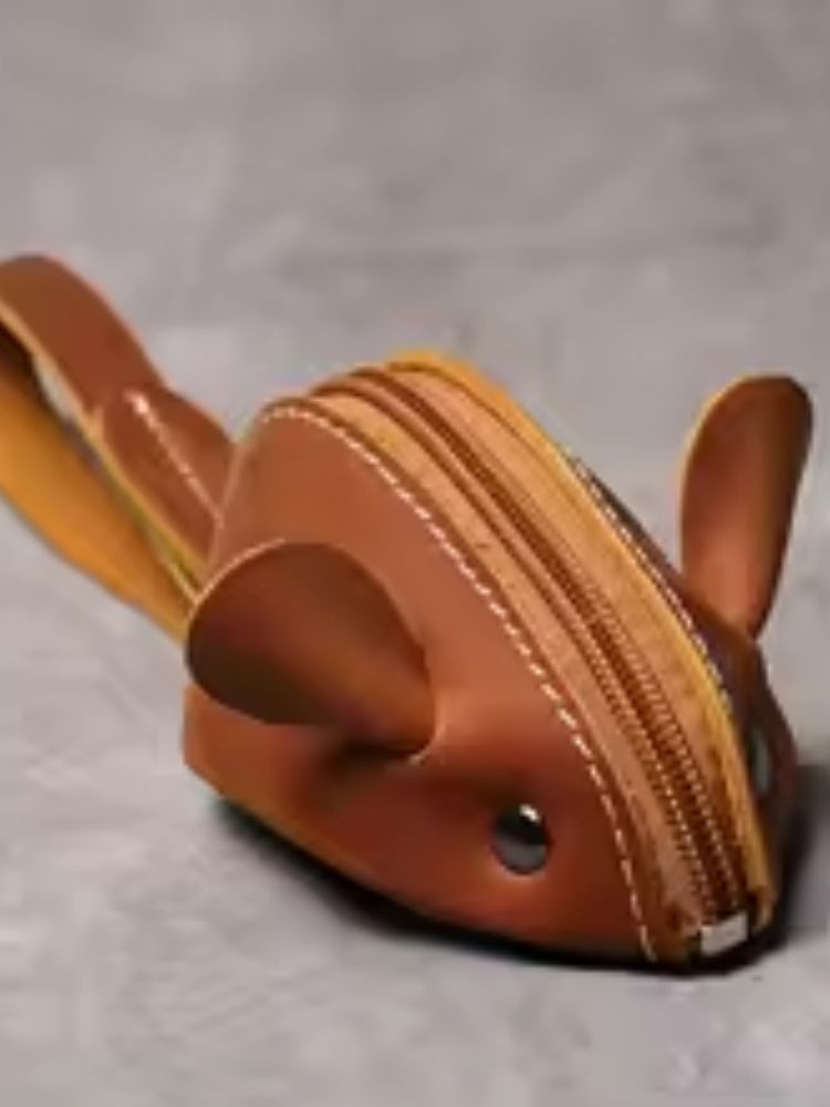 Bolsa pequena em formato de ratinho feita em couro caramelo com zíper amarelo e orelhas arredondadas
