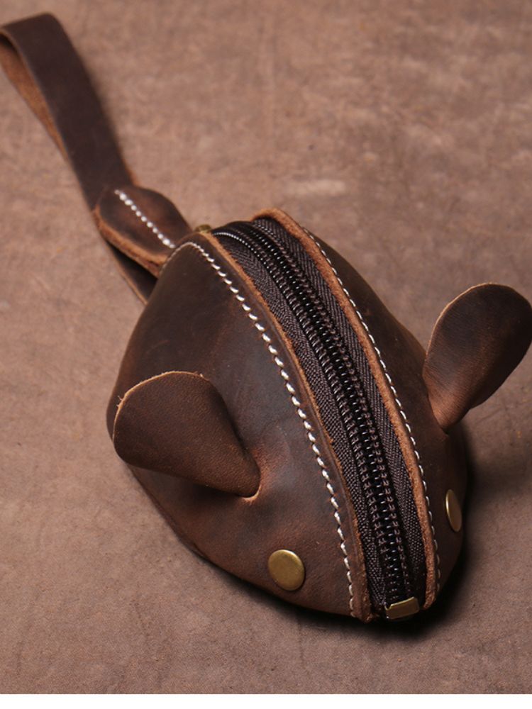 Bolsa pequena em formato de ratinho feita em couro marrom escuro com zíper central e rebites metálicos

