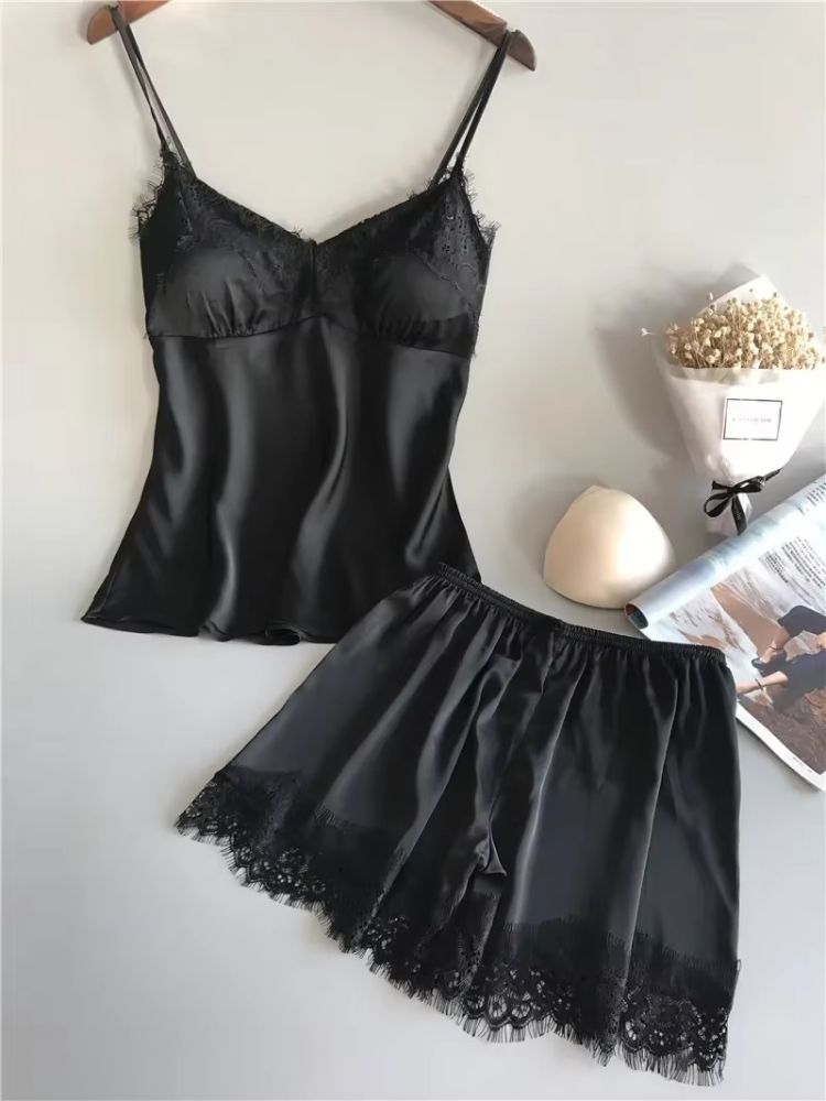 Pijama feminino preto em cetim com top de alças e renda preta no busto, acompanhado de short preto com barra em renda delicada.