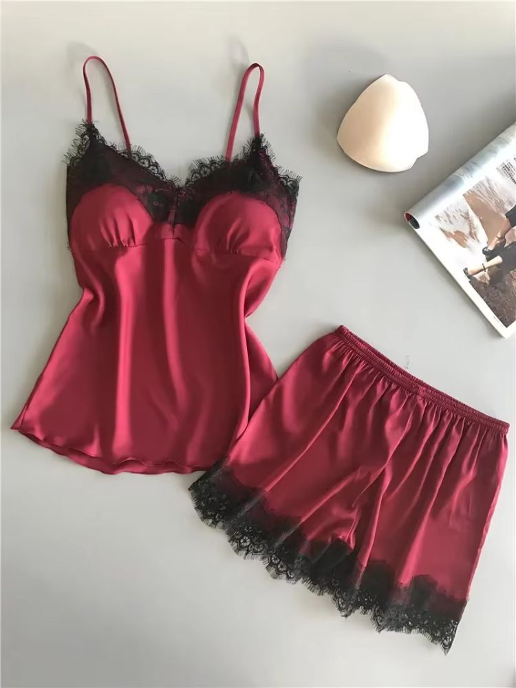 Conjunto de pijama feminino em cetim vinho com top de alças finas e renda preta no busto, acompanhado de short vinho com barra em renda preta sobre superfície clara.