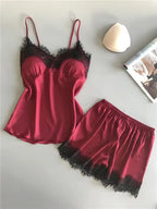 Conjunto de pijama feminino em cetim vinho com top de alças finas e renda preta no busto, acompanhado de short vinho com barra em renda preta sobre superfície clara.