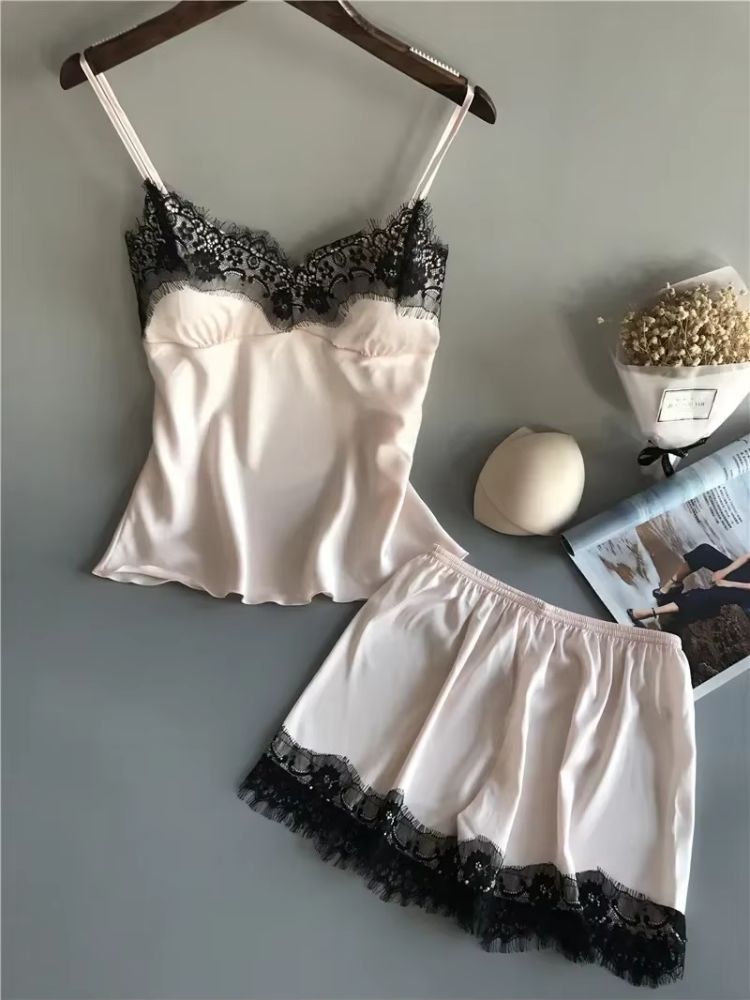 Pijama feminino em cetim bege com top de alças finas e renda preta no decote, acompanhado de short bege com aplicação de renda preta na barra.