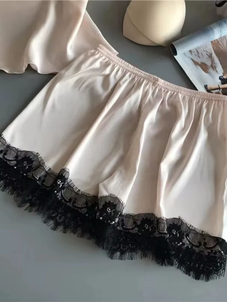 Detalhe do short de cetim bege com acabamento em renda preta na barra, mostrando textura fluida do tecido.