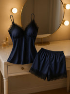 Pijama feminino em cetim azul marinho com renda preta exposto sobre penteadeira iluminada, destacando brilho do tecido e acabamento delicado.