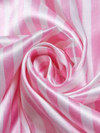 Close do tecido de cetim rosa listrado demonstrando brilho, textura suave e caimento fluido.