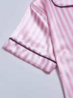 Detalhe da manga do pijama de cetim rosa listrado com vivo preto no acabamento.