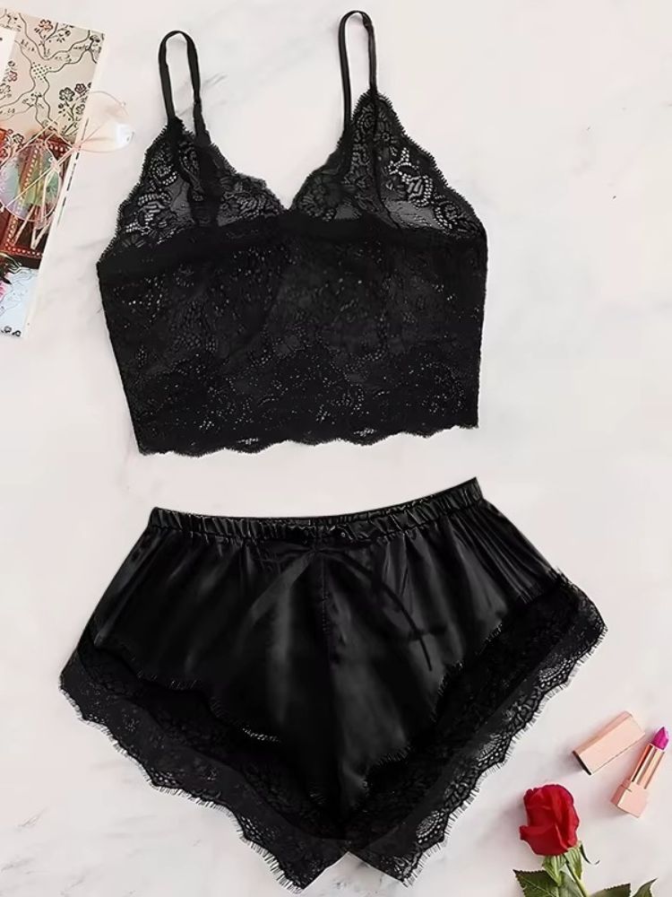 Conjunto de pijama feminino preto com top de renda e shorts de cetim preto com renda nas barras, colocado sobre superfície clara com rosa vermelha.