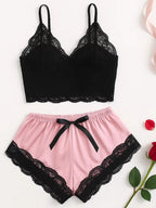 Conjunto de pijama feminino composto por top preto de renda com alças finas e shorts rosa com renda preta na barra e laço na cintura, disposto sobre superfície branca.