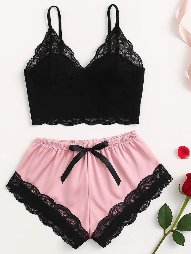 Conjunto de pijama feminino composto por top preto de renda com alças finas e shorts rosa com renda preta na barra e laço na cintura, disposto sobre superfície branca.