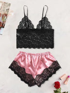 Conjunto de pijama feminino com top preto rendado e shorts rosa acetinado com renda preta, disposto sobre fundo claro com rosa vermelha ao lado.