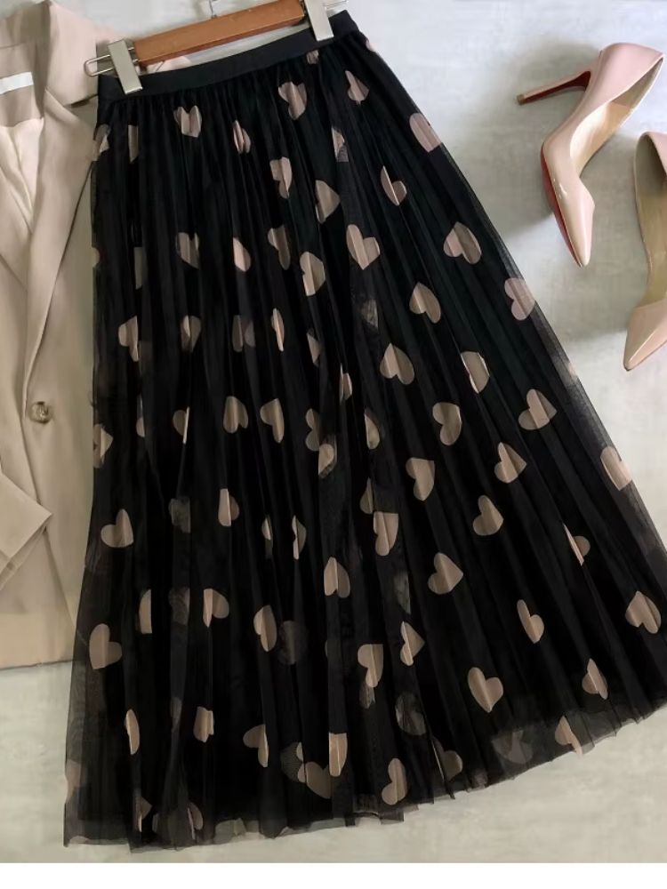 Saia longa de tule preta com corações bege estendida ao lado de blazer e sapatos nude.