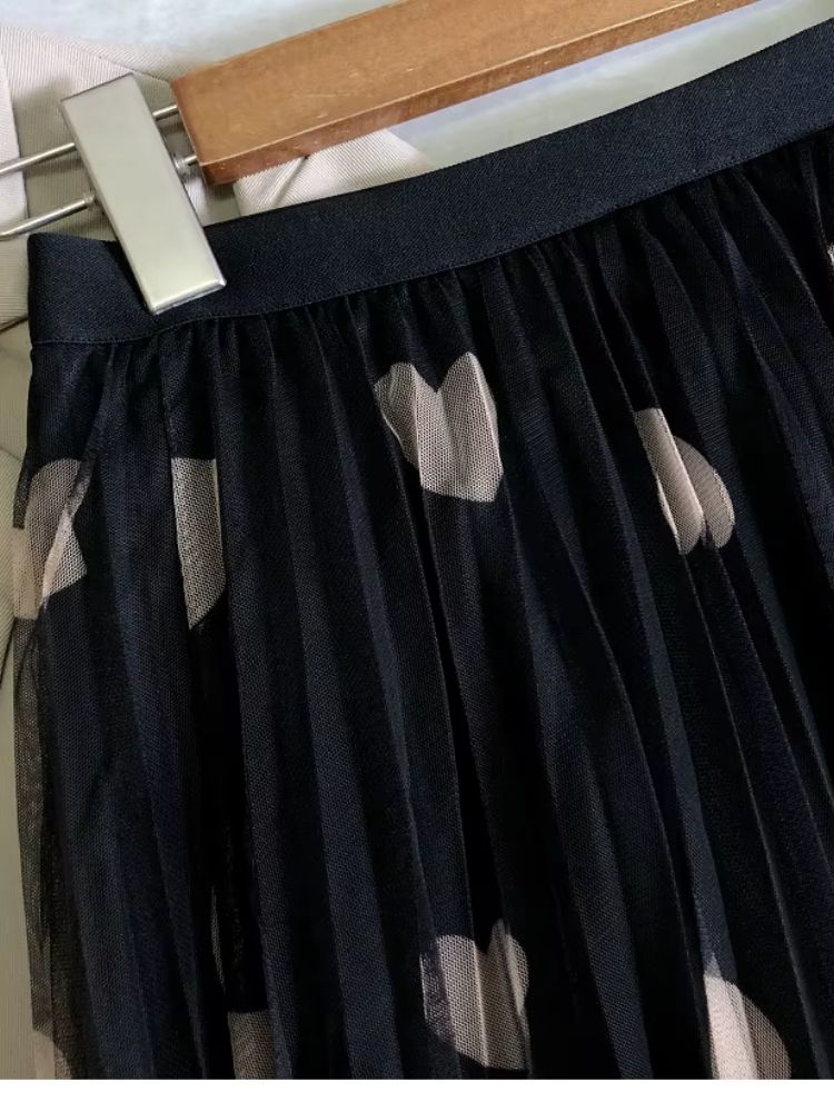 Detalhe da cintura de saia preta de tule com pregas e corações bege pendurada em cabide.