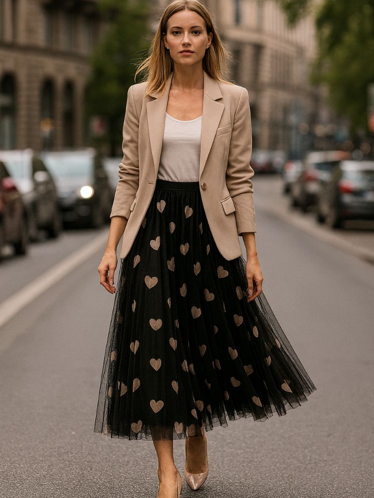 Saia longa de tule preta com estampa de corações bege, combinada com blazer bege e blusa branca em rua da cidade.