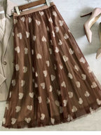 Saia longa de tule marrom com estampa de corações creme estendida sobre superfície plana.