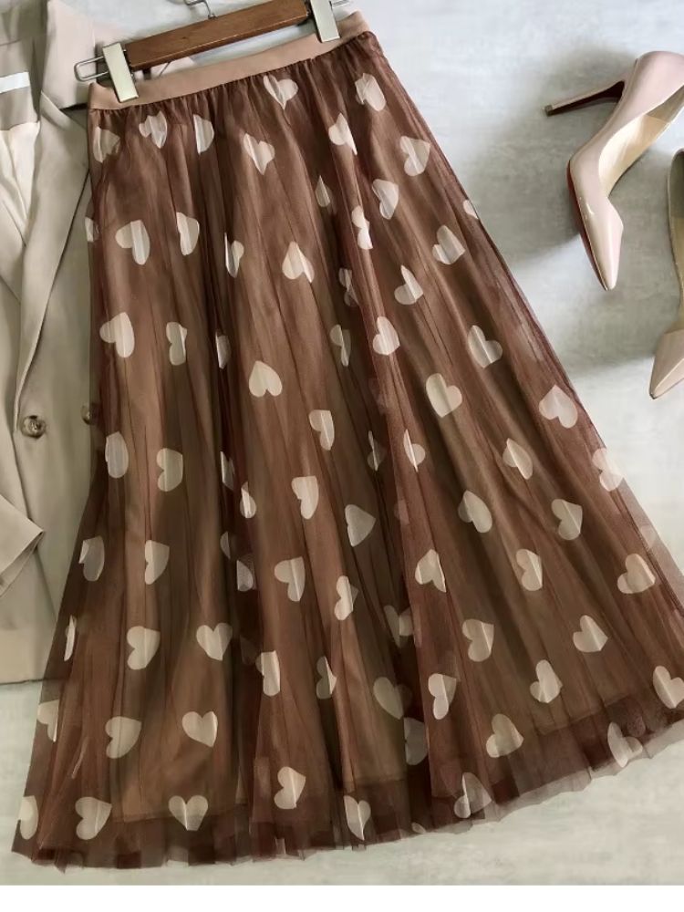 Saia longa de tule marrom com estampa de corações creme estendida sobre superfície plana.