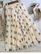 Saia longa de tule bege com estampa de corações cinza clara estendida sobre superfície plana.