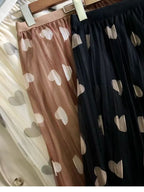 Três saias longas de tule com estampa de corações — bege, marrom e preto — penduradas lado a lado em cabides.