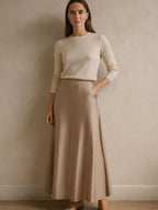 Saia midi nude em cetim com caimento sofisticado, usada com blusa de tricô bege em produção minimalista.