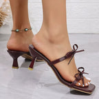 Sandália vinho com bico quadrado e laços frontais, detalhe do salto médio e acabamento brilhante, fotografada em ângulo lateral.