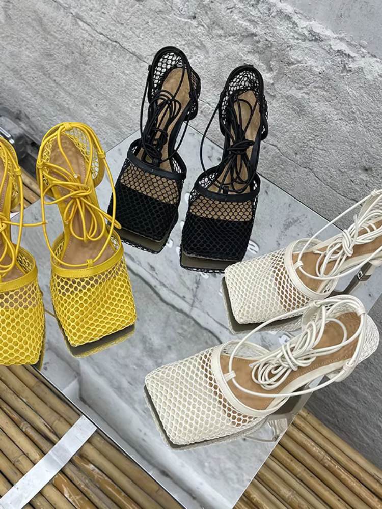 Sandálias femininas de tela vazada nas cores amarelo, preto e branco sobre mesa espelhada, modelo com tiras para amarrar.