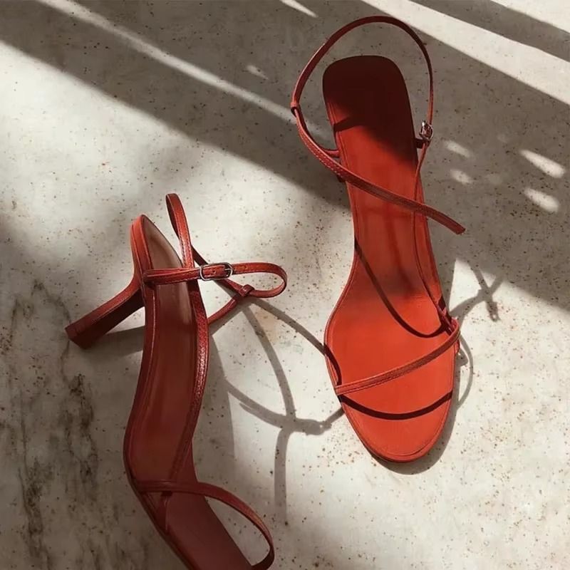 Sandália feminina vermelha com tiras cruzadas e acabamento brilhante em destaque sob luz natural.
